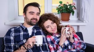 happy young couple sitting on sofa with cups of tea or coffee